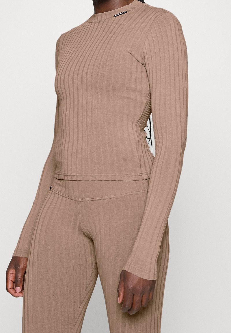 Brązowa prążkowana bluzka z długim rękawem, okrągłym dekoltem i rozcięciami po bokach, w połączeniu z dopasowanymi prążkowanymi legginsami, prezentująca elastyczną tkaninę i dopasowany krój.