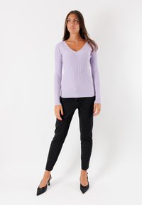 Top a maniche lunghe a coste di colore viola chiaro con scollo a V, abbinato a pantaloni neri slim-fit e décolleté neri a punta.