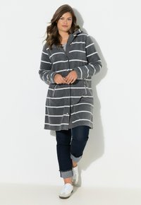 Felpa lunga a righe grigie e bianche realizzata in tessuto morbido, con zip frontale, due tasche laterali e cappuccio con coulisse. Abbinata a jeans scuri.