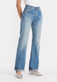 Jeans de tiro alto azul claro con corte recto, textura desteñida y costuras en contraste. Cuenta con cinco bolsillos y trabillas para el cinturón.