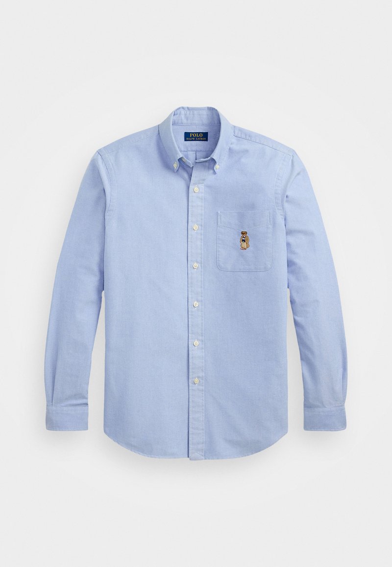 Camisa de botón azul claro hecha de algodón, que presenta un bolsillo en el pecho con un diseño de oso bordado y un cuello clásico.