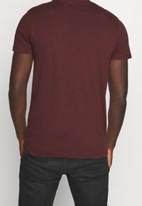 Camiseta de manga corta burdeos hecha de algodón, con cuello redondo y un diseño liso de corte regular. Combinada con jeans oscuros.
