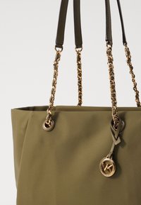 Olivově zelená taška přes rameno s hladkým textilním povrchem, dvojitými koženými a řetízkovými popruhy a akcentem ve formě zlatého loga na straně.