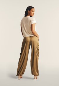 Pantalones cargo sueltos de color caqui con bolsillos laterales, combinados con una blusa beige de manga corta, que presenta un corte relajado y una textura suave.