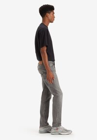 Black short-sleeve t-shirt, gray slim-fit jeans, and gray sports sneakers. Model stands sideways with a textured fabric appearance.