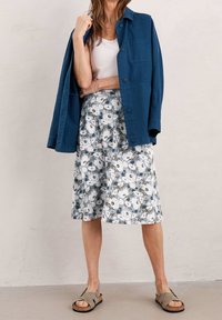 Veste bleu boutonnée sur un débardeur blanc, accompagnée d'une jupe midi à imprimé floral dans des tons de bleu clair et blanc. Porte avec des sandales grises.