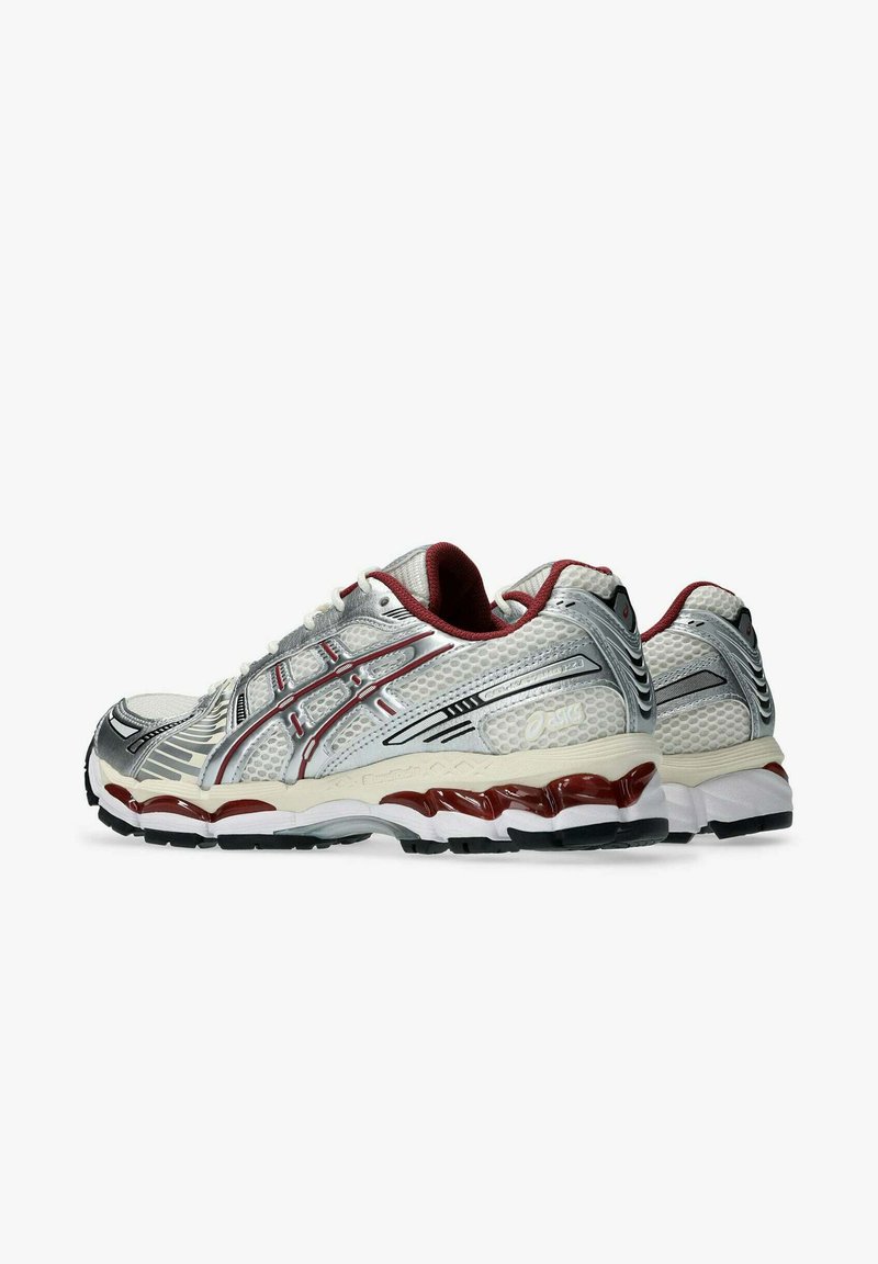 Un paio di scarpe da corsa bianche e argento con accenti rossi e neri, parte superiore in rete e suole spesse e imbottite, mostrate da angolazioni laterali e posteriori.