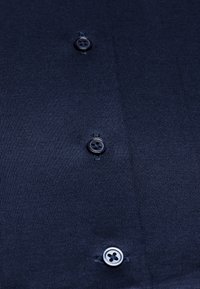 Camicia blu navy con una finissima texture a coste, caratterizzata da tre bottoni neri con design a quattro fori, cuciti su una parte frontale pulita.