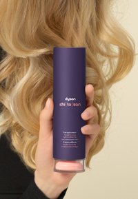 Crema pre-styling Dyson Chi to San in un contenitore cilindrico viola con base trasparente, con etichette di testo bianche e rosa.