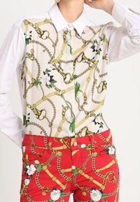 Skjorta med långa ärmar och vit krage, med ett kedje- och blommönster på framsidan. Röda byxor med ett liknande mönster, guldaccentuerade.