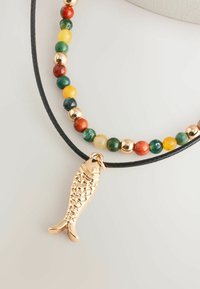 Collier en perles multicolores avec un pendentif en forme de poisson en or. Les perles comprennent du vert, du rouge, du jaune et de l'or sur un cordon tressé noir.