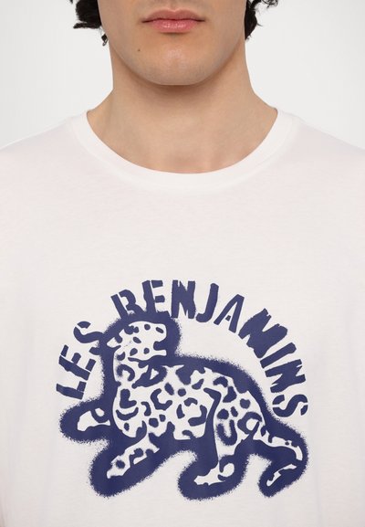 Λευκό μπλουζάκι από βαμβάκι με στρογγυλή λαιμόκοψη, που διαθέτει μια μπλε λεοπάρ γραφικά και κείμενο "LES BENJAMINS" σε έντονη, καμπυλωτή γραμματοσειρά.