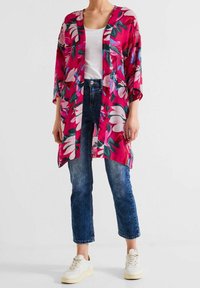 Kwiatowy żakiet kimono w odcieniu różowym, z dużymi rękawami i otwartym przodem. Noszony na białej bluzce z niebieskimi dżinsami i białymi trampkami.