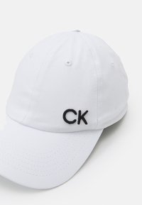 Șapcă de baseball din bumbac alb, cu logo-ul brodat „CK” negru în față; are un visor curbat și orificii de ventilație.