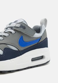 Sneaker Nike grigia, blu scuro e blu con suola bianca, logo swoosh blu, lacci grigi e dettagli in tessuto a rete.