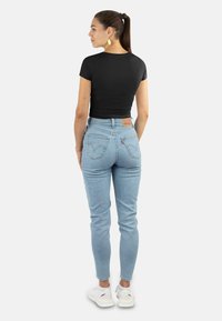Schwarzes, eng anliegendes T-Shirt mit kurzen Ärmeln, kombiniert mit hellblauen, hochgeschnittenen Jeans. Texturiertes Material, Fünf-Taschen-Design und ein Lederaufnäher auf der Rückseite.