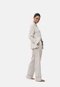 Ensemble de détente beige comprenant une chemise à col et boutons ainsi que des pantalons à jambes larges, fabriqué dans un tissu doux avec des bordures contrastantes aux poignets et à l'ourlet.