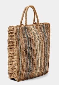 Torba na zakupy z plecionej słomy z dwoma uchwytami, ozdobiona pionowymi paskami w kolorach beżowym, niebieskim i zielonym. Teksturowana powierzchnia o prostokątnym kształcie.