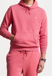 Sudadera de algodón rosa con bolsillo tipo canguro, capucha ajustable con cordón, puños de canalé y un pequeño logo bordado en el pecho.
