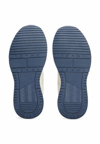 Niebieskie gumowe podeszwy z teksturowanym gripem, z wyraźnymi wzorami w jodełkę i okrągłymi bieżnikami. Wygrawerowane litery "TOMMY JEANS".