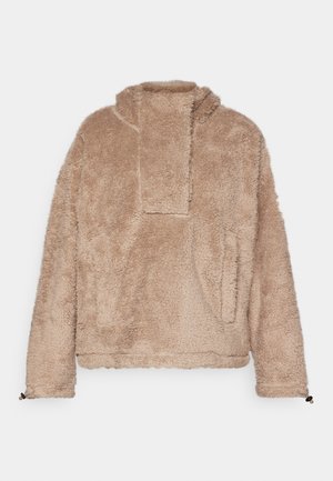 Pulover bej pufoș, cu guler înalt, având un design cu umeri lăsați și buzunare laterale. Material texturat cu un aspect moale și pufos.