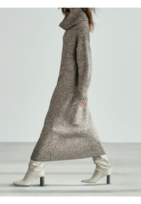 Robe pull longue en tricot beige avec un grand col montant texturé. Elle présente de longues manches et un dégradé de couleur vers des tons plus clairs.