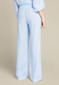 Pantaloni azzurri chiari a gamba larga con strisce bianche verticali, cintura elastica e texture di tessuto morbido, mostrati da dietro.