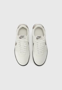 Nike shoes in white with gray accents, featuring a smooth synthetic upper, round toe, and flat black outsole. Lace-up design with logo tag.