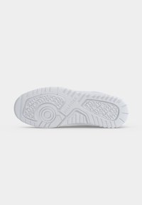 Semelle d'une basket blanche avec des motifs de grip texturés et le nom de la marque "Hilfiger" embossé au centre.