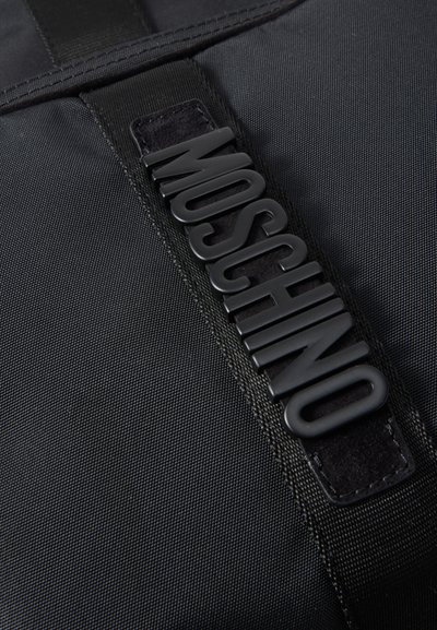 Μαύρο υφασμάτινο με υφή, με μια μαύρη ελαστική ετικέτα λογότυπου Moschino ραμμένη σε μαύρη υφασμάτινη λωρίδα.