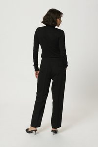 Zwarte coltrui en zwarte op maat gemaakte broek, gezien van achteren. Soepele textuur met minimale naden. Schoenen: zwarte open teen hakken.