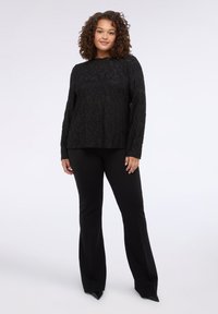 Schwarzes Langarmoberteil mit strukturiertem Blumenmuster, kombiniert mit engen schwarzen Hosen und spitzen schwarzen Schuhen, die einen monochromen Look kreieren.