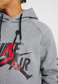 Sudadera gris de tela suave, con un gran gráfico en negro y rojo de "NIKE AIR", capucha con cordones y un corte relajado.