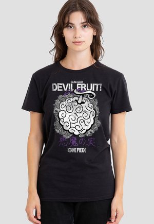 Junge Frau trägt ein schwarzes T-Shirt mit weißem, wirbelndem Fruchtdesign und dem Text "Gum-Gum Devil Fruit" sowie "One Piece" in stilisierten Buchstaben.