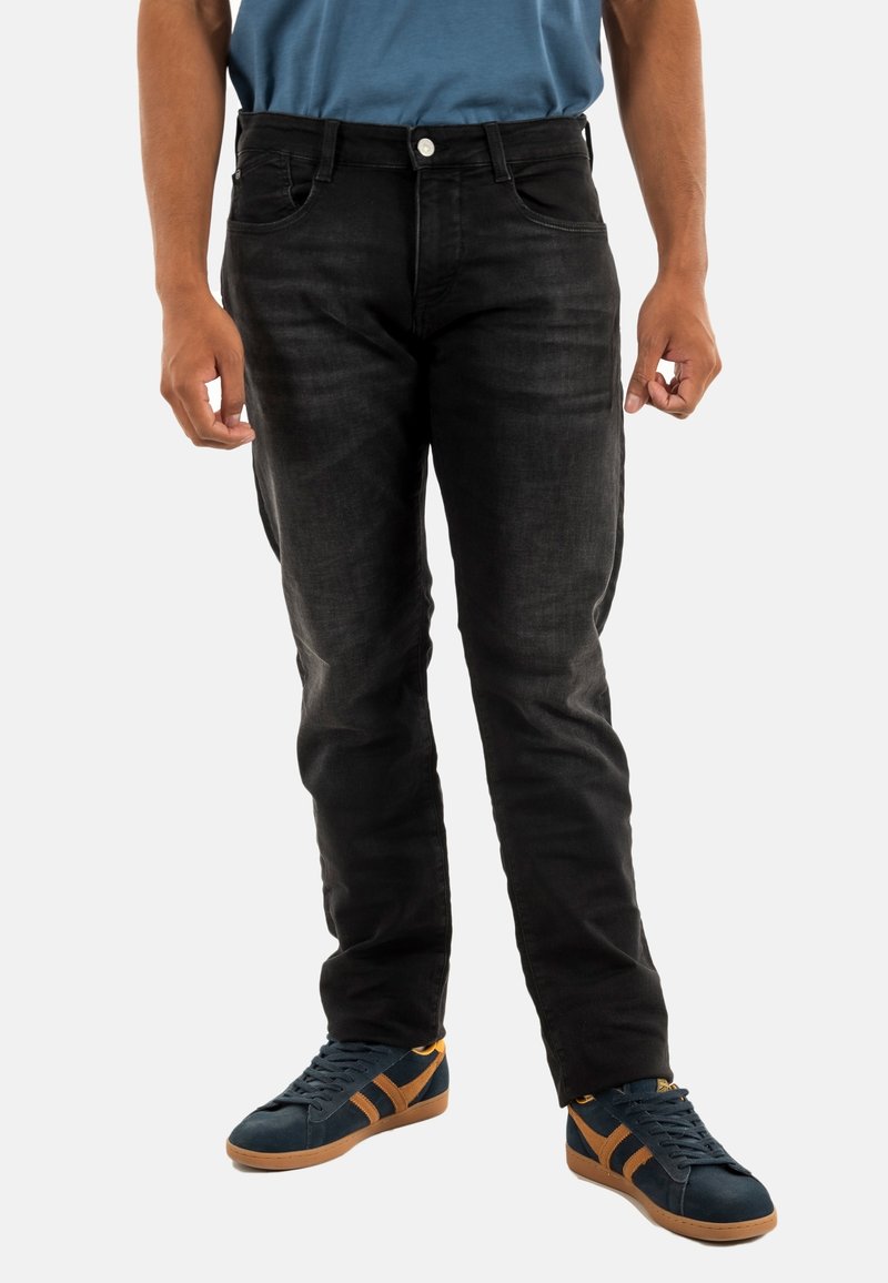 Jeans de mezclilla negra con un corte recto, diseño de cinco bolsillos y un ligero desgaste. Combinados con zapatillas de deporte azul oscuro con franjas naranjas.
