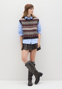 Gebreide vest met rode, witte en zwarte patronen; lichtblauw shirt; bruine leren rok; grijze knie sokken; en bruine kniehoge laarzen.
