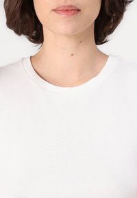 T-shirt en coton blanc avec un col rond, présentant une texture lisse et des détails de couture minimaux, exposé sur un fond neutre.