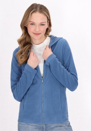 Felpa con zip in morbido blu, dotata di cappuccio, maniche lunghe e chiusura a zip. Indossata sopra una maglietta bianca, con tasche visibili sui lati.