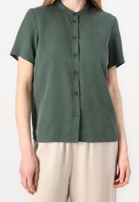 Short-sleeved green button-up shirt in a soft fabric with a collar. Features a straight cut and simple button closure.