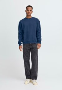 Sudadera de cuello redondo en color navy, hecha de un tejido suave, combinada con jeans gris oscuro y zapatillas de color claro, creando un look relajado y casual.