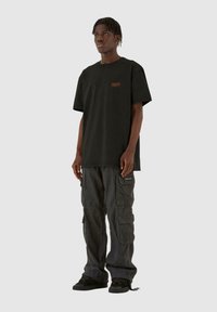 Sort bomulds T-shirt med korte ærmer og rund hals, med et orange logo. Kombineret med grå cargobukser og sorte sneakers.