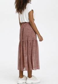 Falda larga y acampanada de un tejido rosa con un patrón de manchas negras. Combinada con una blusa corta y holgada de manga corta blanca y deportivas gruesas blancas.