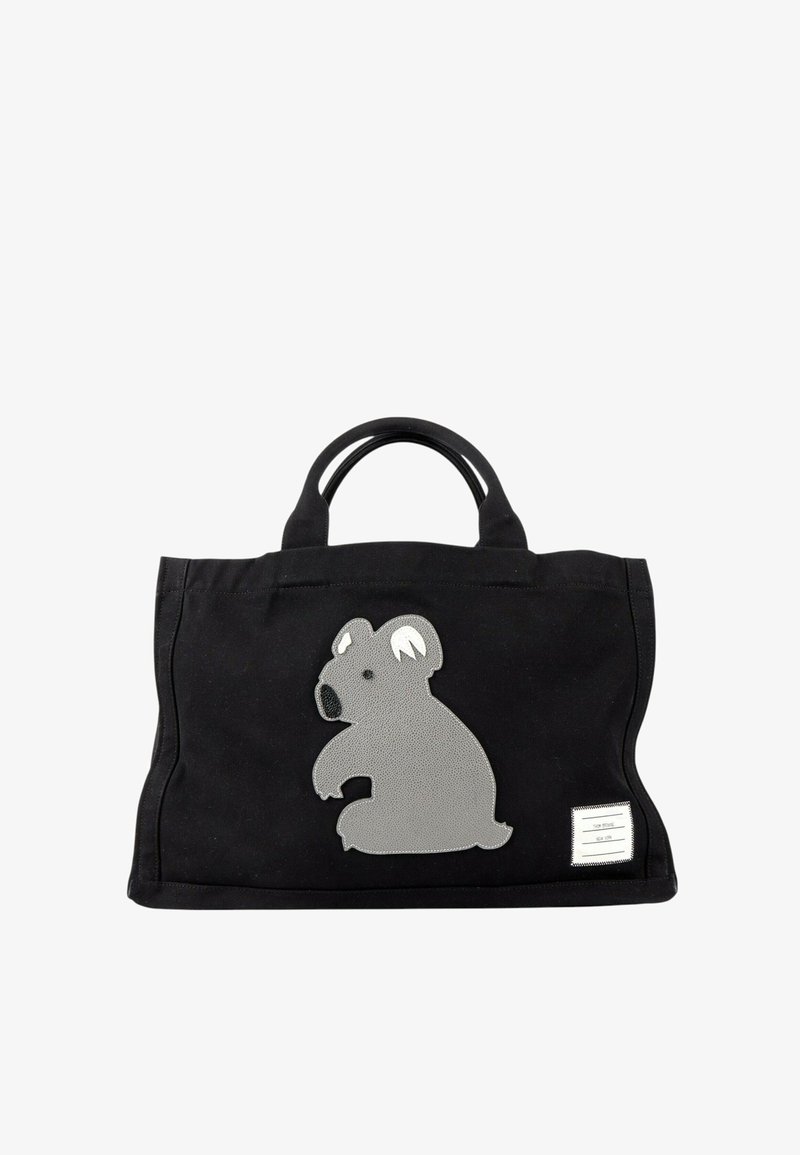 Sac fourre-tout noir avec des poignées courtes et un grand patch koala gris sur le devant, plus une petite étiquette rectangulaire blanche dans le coin inférieur.