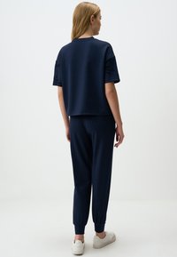 Marineblauw cropped sweatshirt met geborduurde bloemdetails op de mouwen, gecombineerd met bijpassende slanke broek en witte sneakers.