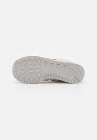 Semelle d'une basket rose clair montrant une bande de roulement en caoutchouc gris texturé avec de petites pastilles rectangulaires et carrées pour l'adhérence et la traction.