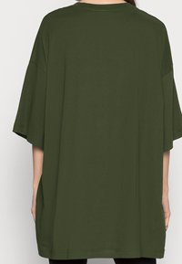 Przestronna, ciemnozielona koszulka bawełniana z krótkimi rękawami, okrągłym dekoltem i luźnym krojem, z minimalnymi detalami przeszycia.