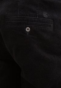Pantalons en velours noir avec une poche arrière ornée d'un bouton en argent décoratif portant l'inscription "BIG STAR". La texture est côtelée et douce.