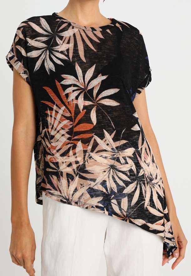 Haut noir à manches courtes avec imprimé de feuilles tropicales beige, rouille et marine, associé à un pantalon blanc, porté par une personne sur un fond uni.
