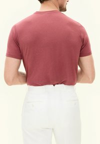 T-shirt a maniche corte e scollo rotondo di un rosa tenue, abbinata a pantaloni bianchi con tasche posteriori e una vestibilità slim. Tessuto morbido e liscio.