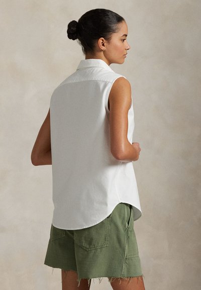 Biela bezrukávová košeľa s golierom a zaobleným lemom; doplnená zelenými šortkami s textúrovaným povrchom a rozstrapkanými okrajmi. Jednoduchý dizajn.